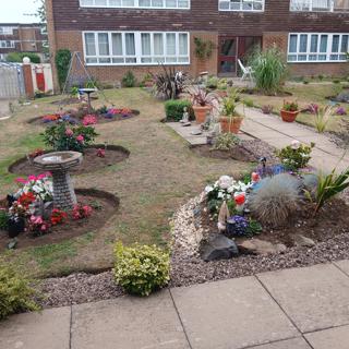 A tidy front communal garden with circular bedding borders with flowers and lawn