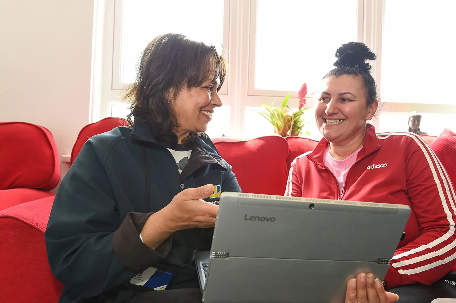 A Wolverhampton Homes team member with a laptop on a red sofa, talking to a customer