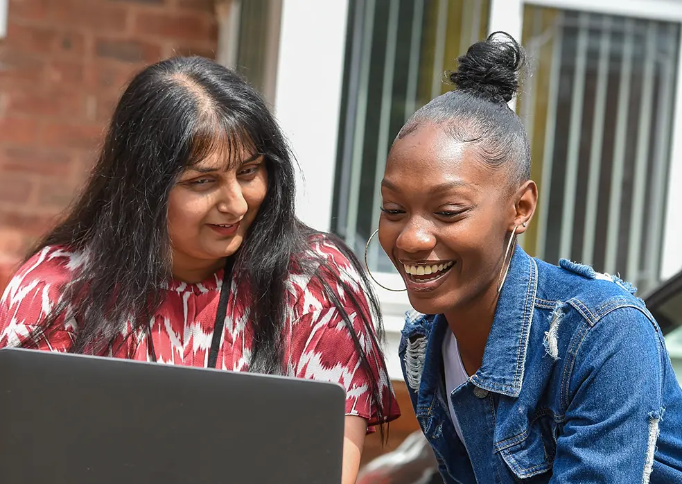 A young woman in a denim jacket looks at a laptop with a Wolverhampton Homes team member