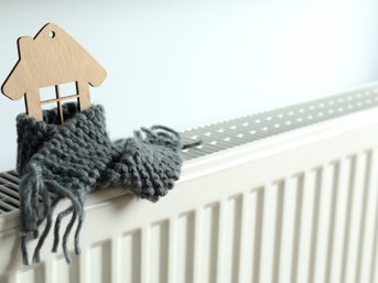 A radiator on top of which is a miniature house wrapped in a scarf