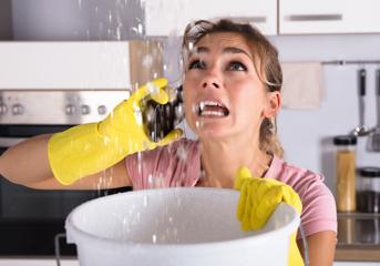 A woman with water leaking form her ceiling, on the phone