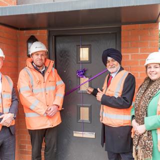 Four people in hi-vis jackets at one of the new-build properties, cutting a purple ribbon on a black front door