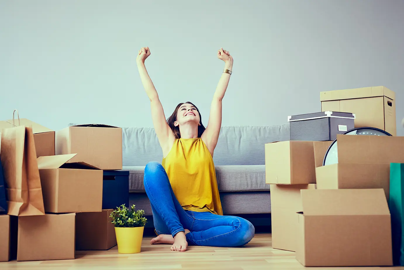 A woman sits on the carpet, surrounded by cardboard boxes