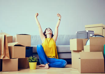 A woman sits on the carpet, surrounded by cardboard boxes