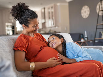 A pregnant woman sits with her child on a sofa