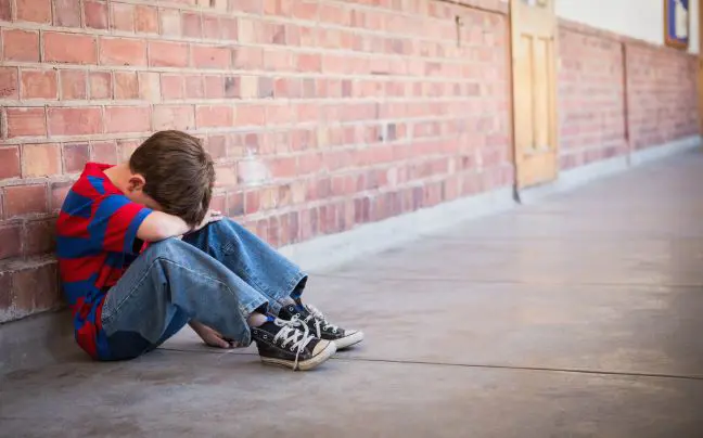 A child, sitting on the ground, with his head resting on his arms