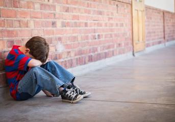 A child, sitting on the ground, with his head resting on his arms
