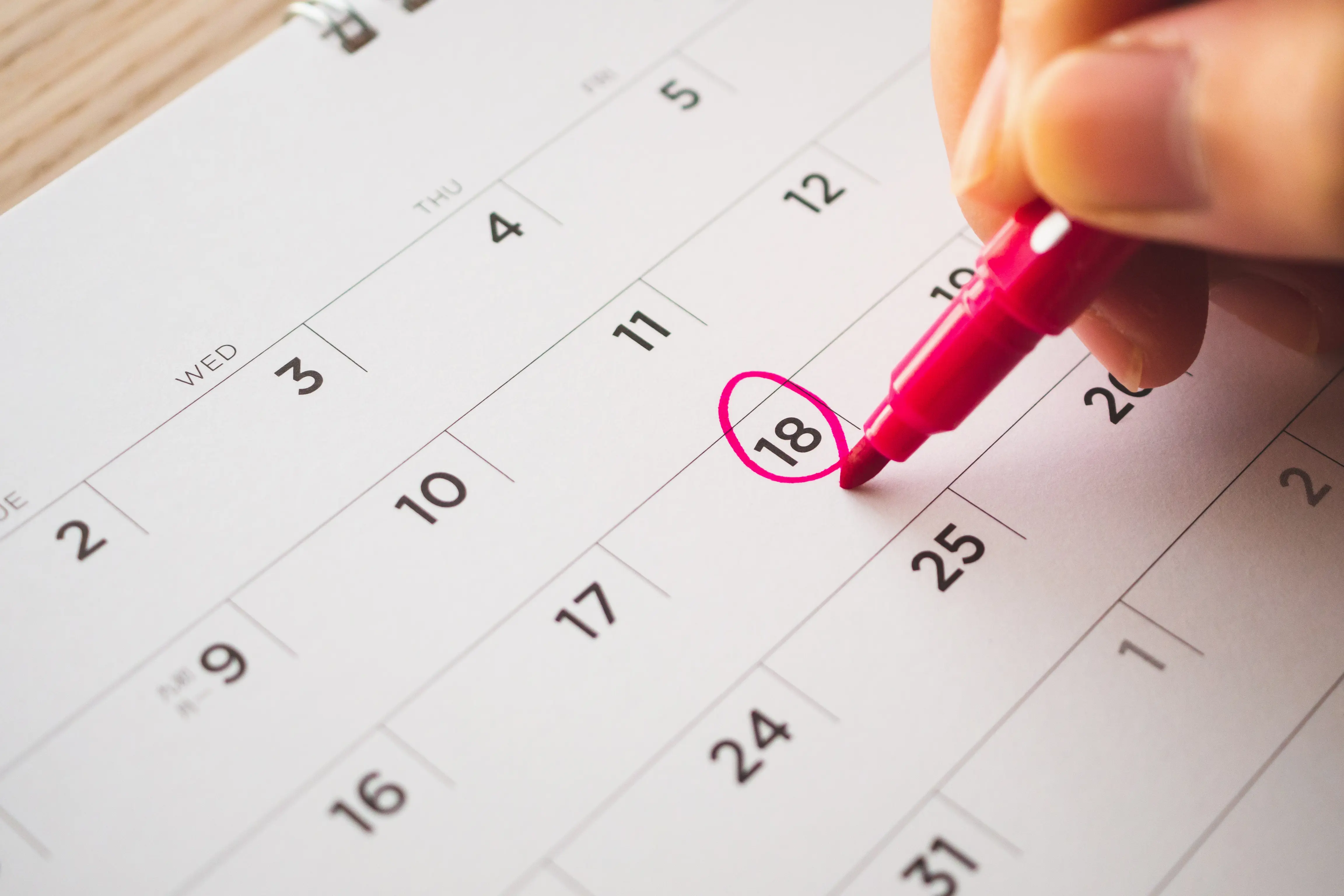 A calendar with someone circling a date with a red pen
