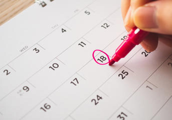 A calendar with someone circling a date with a red pen