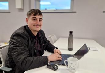 A Wolverhampton Homes apprentice sits at a desk with a mug and laptop