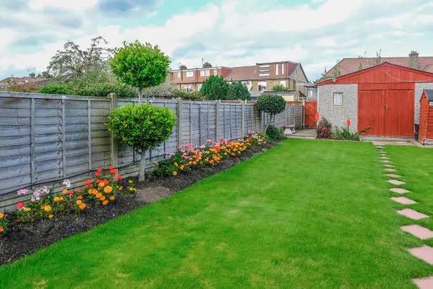 A neat garden with grass, flowers and a fence