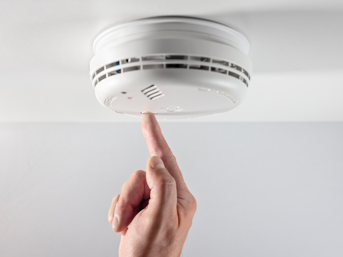 A hand tests a smoke alarm