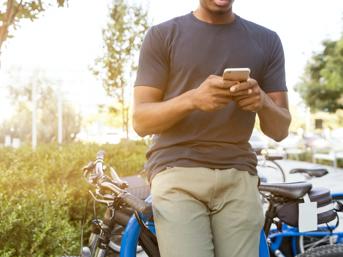 A man leans against his bicycle and looks at his mobile phone