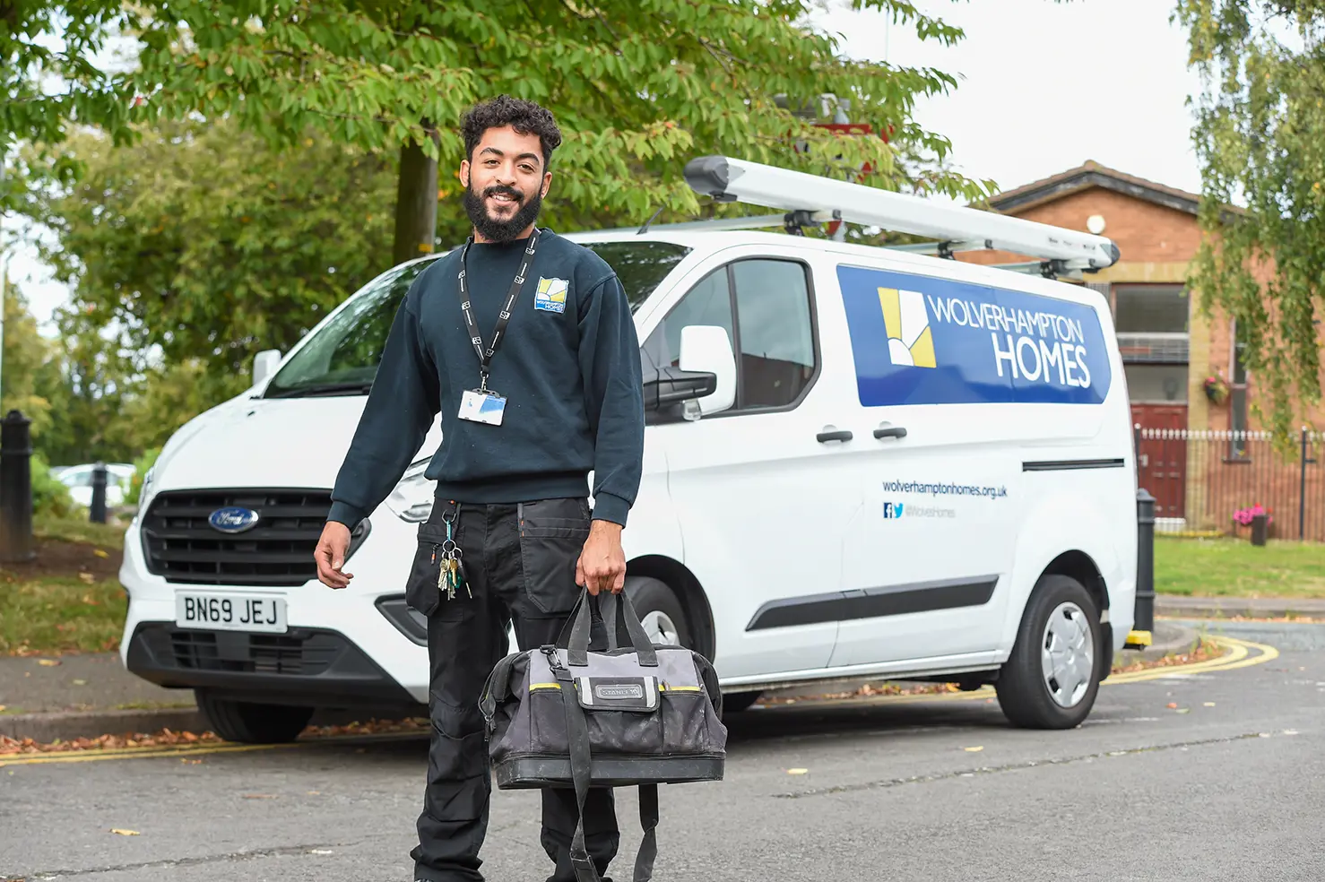 A Wolverhampton Homes operative with a bag in his hand, standing by a WH van