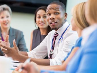 A man in a shirt and tie talks to four women in a meeting