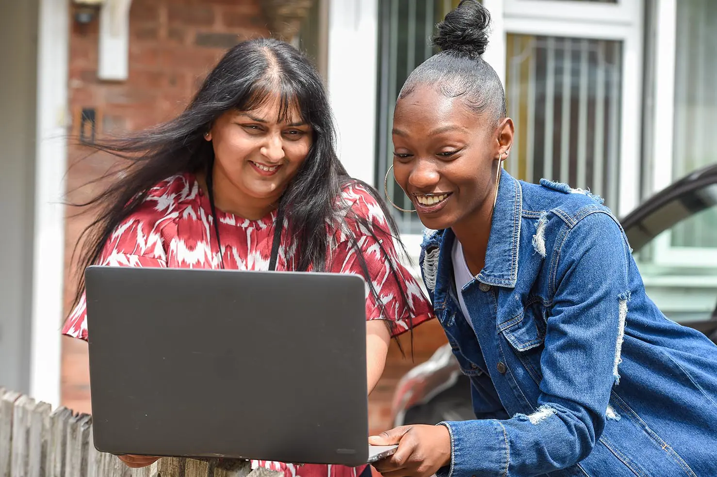 A young woman in a denim jacket and a Wolverhampton Homes team member look at a laptop outside