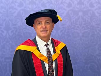 Portrait of a Shaun Aldis in academic dress and cap