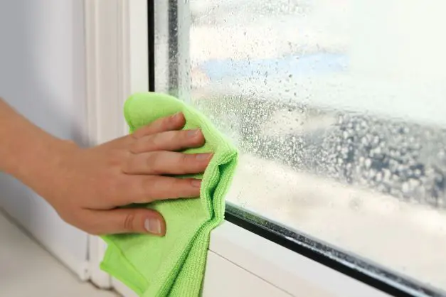 Hand wiping condensation from a window with a cloth
