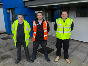 Three men from United Living, wearing hi-vis jackets, outside flats in Heath Town