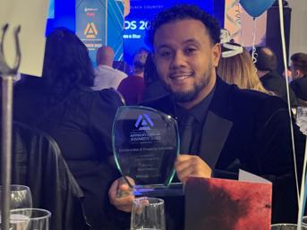 A Wolverhampton Homes apprentice at an awards ceremony, holding the Apprenticeship Awards 2023 trophy