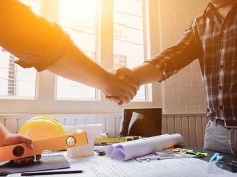 Two people, shaking hands over a table with paperwork