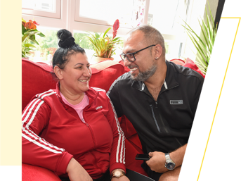 A couple on a red sofa, smiling at each other 